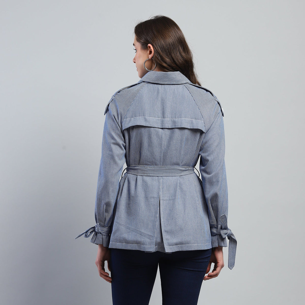 Woman wearing a gray jacket with a belt on a gray background