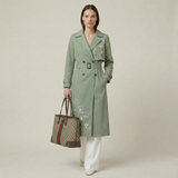 Woman wearing a green trench coat holding a Gucci handbag on a plain background