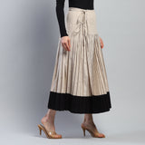 Beige pleated skirt with black bottom section worn by a person on a gray background