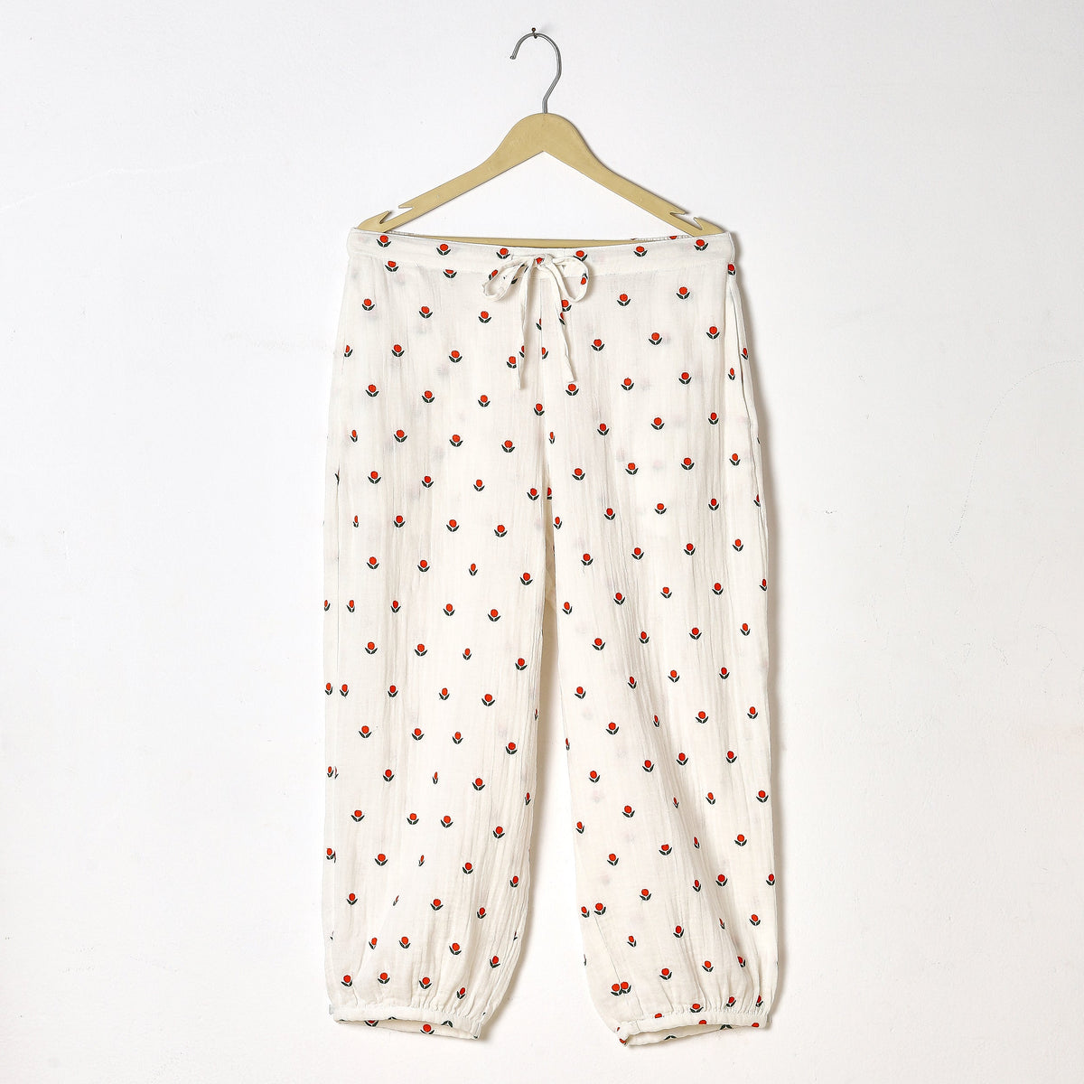 White pants with red floral pattern on a hanger against a white background