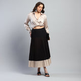 Woman wearing a beige blouse and black pleated skirt on a gray background
