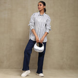 Woman wearing a striped shirt and dark pants, holding a white handbag against a beige background
