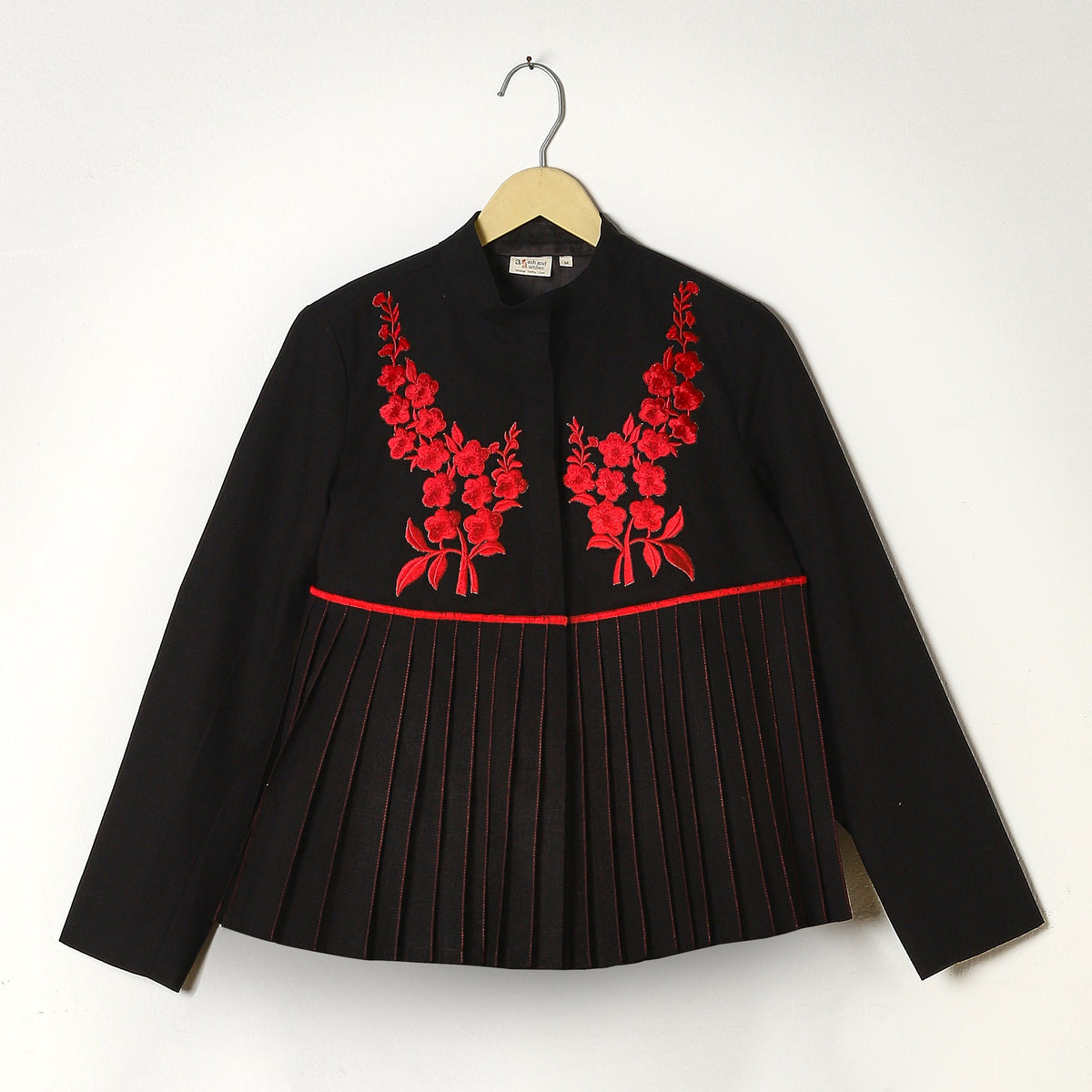 Black blouse with red floral embroidery on a hanger against a white background