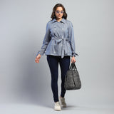 Woman wearing a blue denim jacket and dark jeans, holding a gray handbag on a light gray background