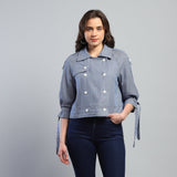 Woman wearing a blue denim jacket with white buttons on a gray background